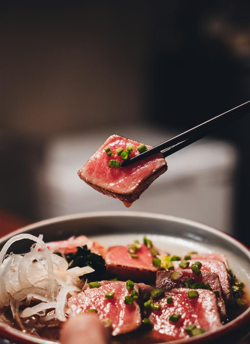 Seared beef tataki held up with chopsticks