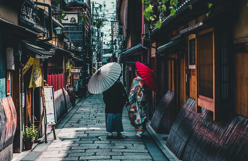 Women in kimono with paper umbrellas walking a Gion alley